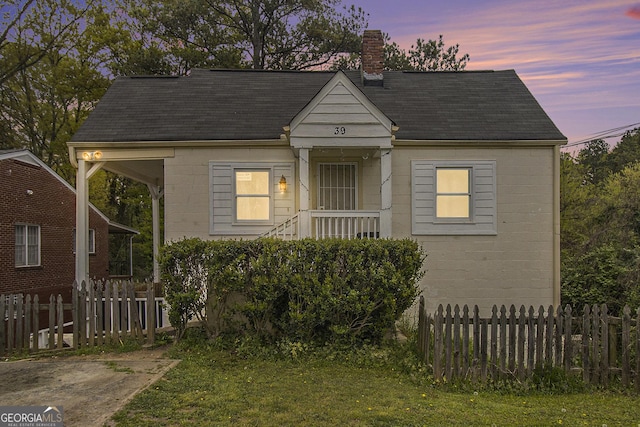 bungalow-style home featuring a chimney, fence, and concrete block siding