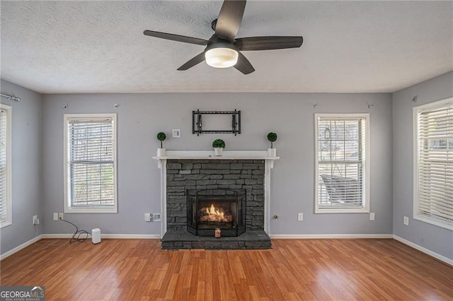 190 The Falls Blvd, Covington, GA 30016 - unfurnished living room with wood finished floors, a stone fireplace, healthy amount of natural light, and a textured ceiling
