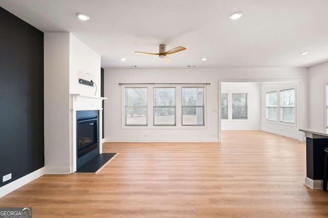 unfurnished living room with light wood-style floors, a fireplace with flush hearth, and plenty of natural light