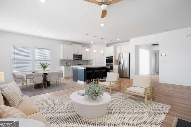 living area featuring ceiling fan, light wood-type flooring, visible vents, and recessed lighting