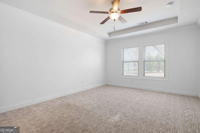 carpeted empty room with a tray ceiling, a ceiling fan, visible vents, and baseboards