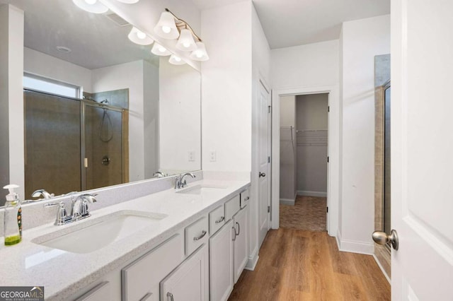 full bathroom with a stall shower, a walk in closet, a sink, and wood finished floors