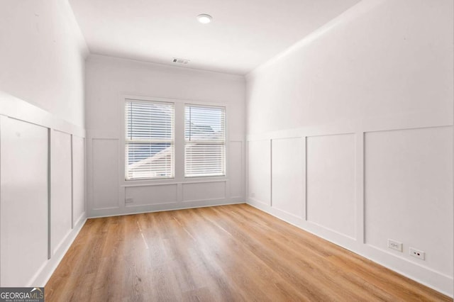 spare room with light wood-style flooring, wainscoting, visible vents, and a decorative wall