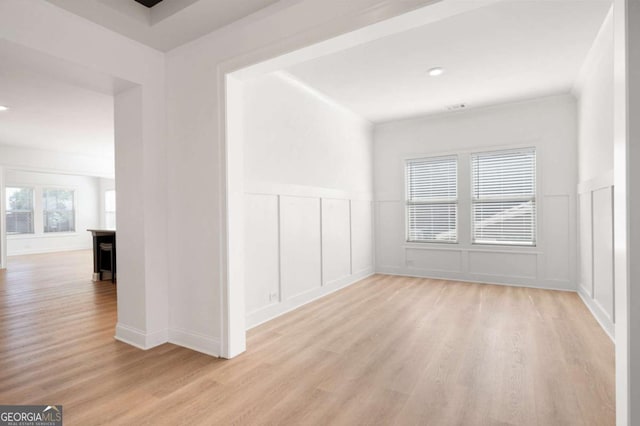 spare room with wainscoting, a decorative wall, and light wood-style flooring