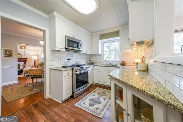 kitchen with dark wood finished floors, appliances with stainless steel finishes, a fireplace, white cabinets, and a sink