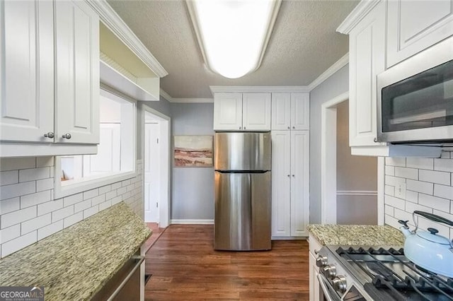 kitchen with ornamental molding, light stone counters, dark wood finished floors, white cabinetry, and appliances with stainless steel finishes