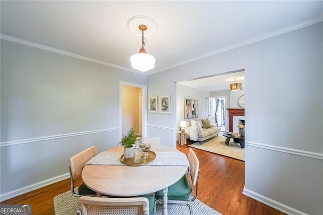 dining area with a fireplace, wood finished floors, baseboards, and ornamental molding