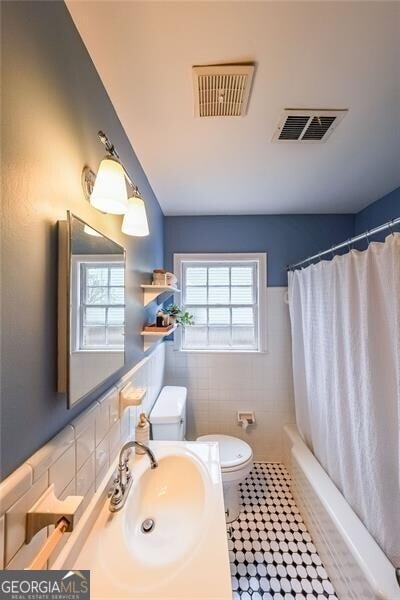 bathroom with visible vents, toilet, tile walls, and shower / bathtub combination with curtain