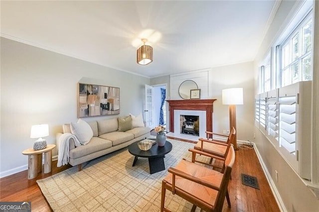 living area with a fireplace with flush hearth, wood finished floors, baseboards, and ornamental molding