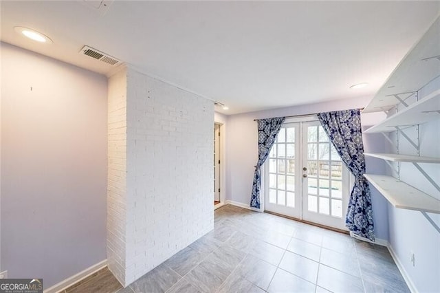 tiled spare room featuring french doors, visible vents, brick wall, and baseboards