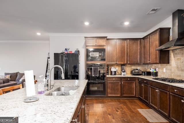 kitchen featuring a sink, visible vents, wall chimney range hood, backsplash, and black appliances