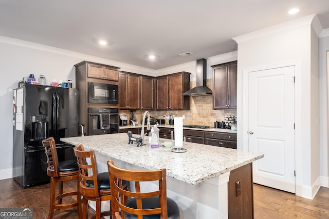 kitchen with dark brown cabinetry, wall chimney range hood, decorative backsplash, light stone countertops, and black appliances