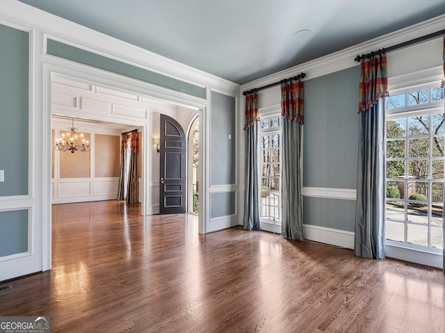 unfurnished room featuring crown molding, visible vents, a decorative wall, wood finished floors, and a chandelier