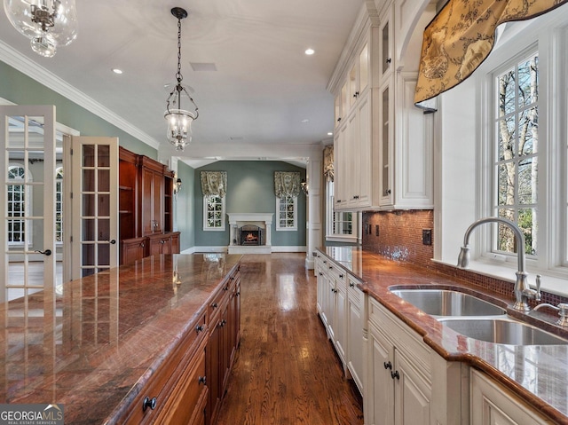 kitchen featuring ornamental molding, glass insert cabinets, open floor plan, a sink, and a lit fireplace