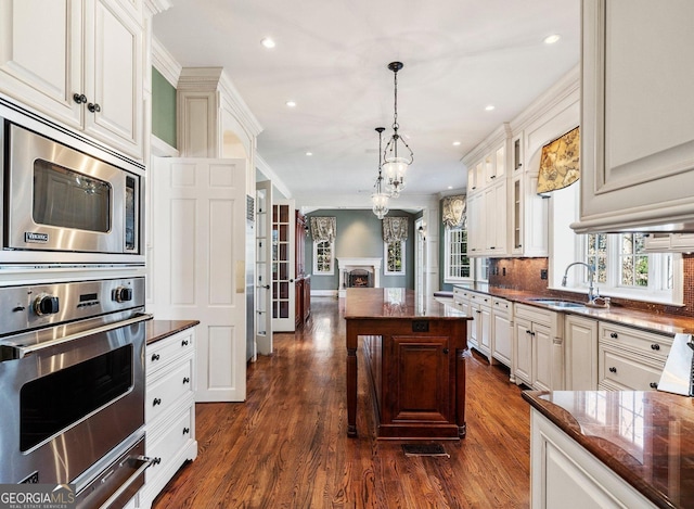 kitchen with stainless steel appliances, decorative backsplash, ornamental molding, a sink, and a warm lit fireplace