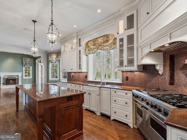 kitchen with a warm lit fireplace, range with two ovens, dark wood-type flooring, a sink, and hanging light fixtures