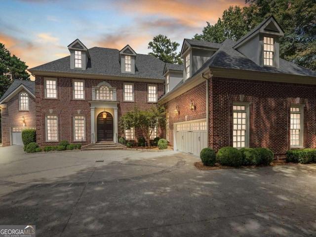 colonial inspired home with driveway, roof with shingles, a garage, and brick siding