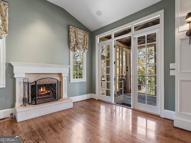 unfurnished living room featuring vaulted ceiling, a warm lit fireplace, wood finished floors, and baseboards