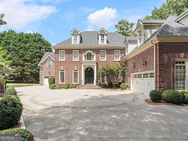 georgian-style home with a shingled roof, brick siding, driveway, and an attached garage