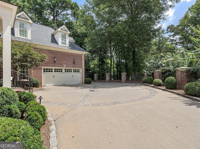 view of property exterior featuring brick siding, roof with shingles, fence, a garage, and driveway