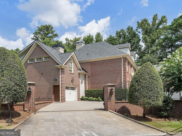 view of front of home with a shingled roof, concrete driveway, a chimney, fence, and brick siding