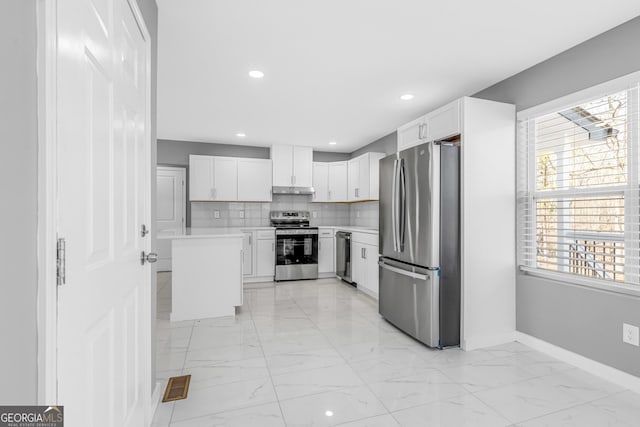 kitchen with under cabinet range hood, stainless steel appliances, marble finish floor, light countertops, and decorative backsplash