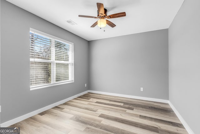 spare room featuring light wood-style floors, a ceiling fan, visible vents, and baseboards