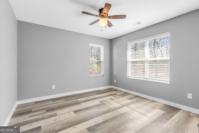 empty room with baseboards, visible vents, ceiling fan, and wood finished floors