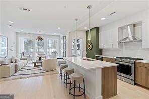 kitchen featuring high end stove, a kitchen island with sink, a sink, light countertops, and wall chimney range hood