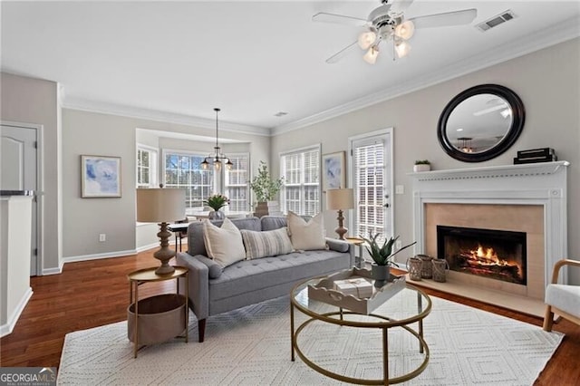 living room with ornamental molding, wood finished floors, visible vents, and baseboards