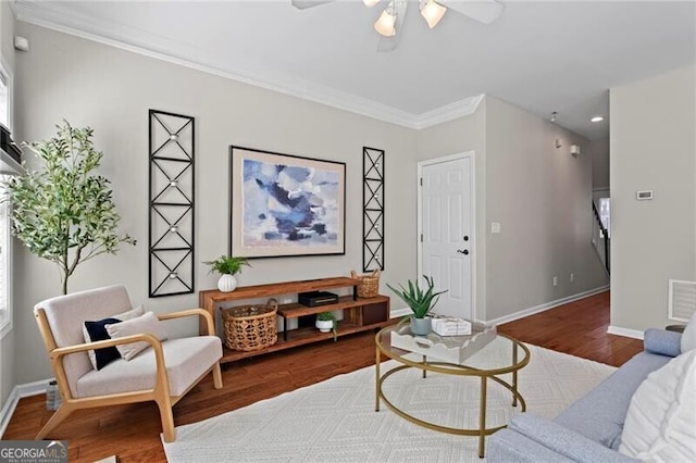 living area with a ceiling fan, crown molding, baseboards, and wood finished floors