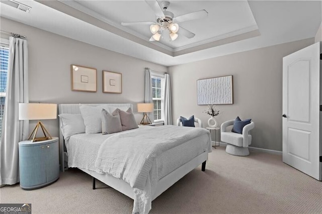 bedroom with a tray ceiling, multiple windows, visible vents, and light colored carpet