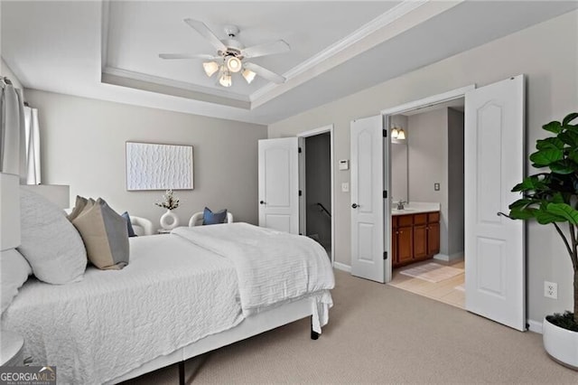 bedroom with a tray ceiling, crown molding, light colored carpet, a sink, and ensuite bath