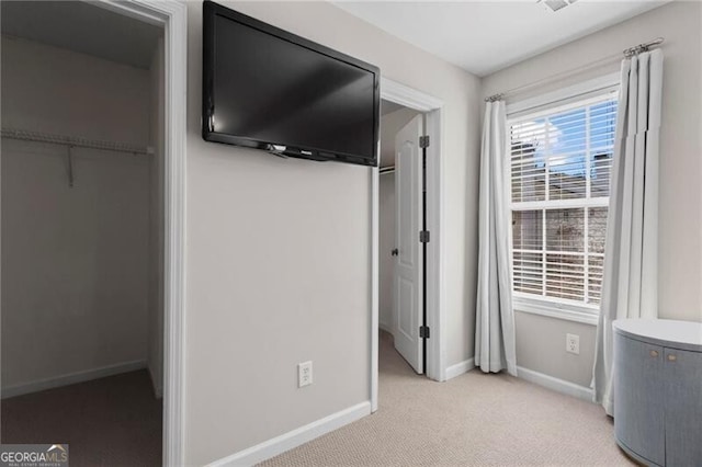 unfurnished bedroom with baseboards, a walk in closet, and light colored carpet