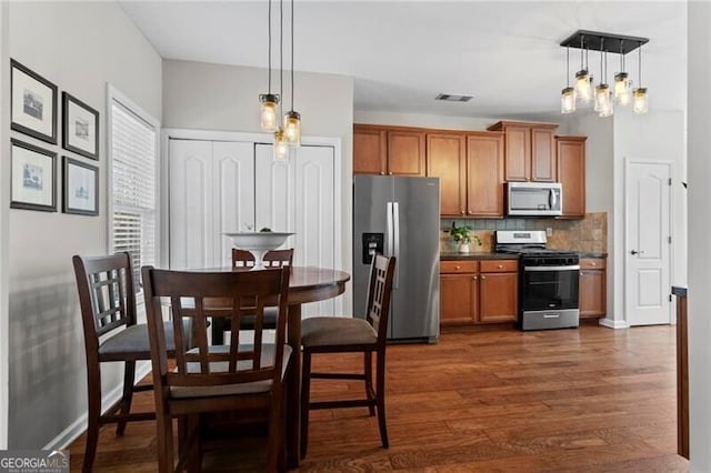 kitchen with visible vents, dark wood finished floors, appliances with stainless steel finishes, brown cabinets, and backsplash