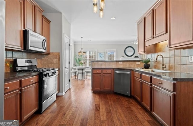 kitchen with stainless steel appliances, a peninsula, a sink, backsplash, and dark wood-style floors