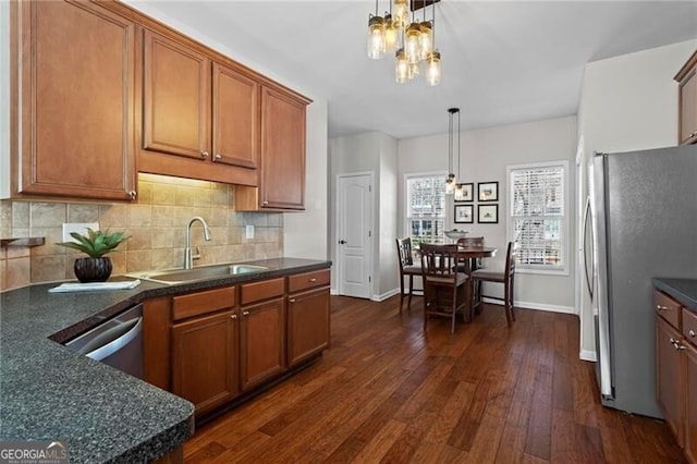 kitchen featuring brown cabinetry, dark countertops, dark wood-style floors, appliances with stainless steel finishes, and a sink