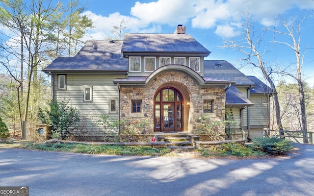 tudor home with stone siding, french doors, and a chimney