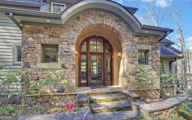 doorway to property featuring stone siding, french doors, and roof with shingles