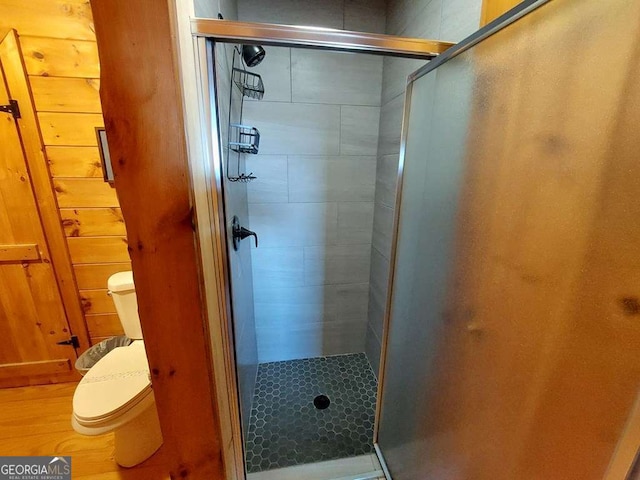 bathroom featuring a stall shower, toilet, and wooden walls