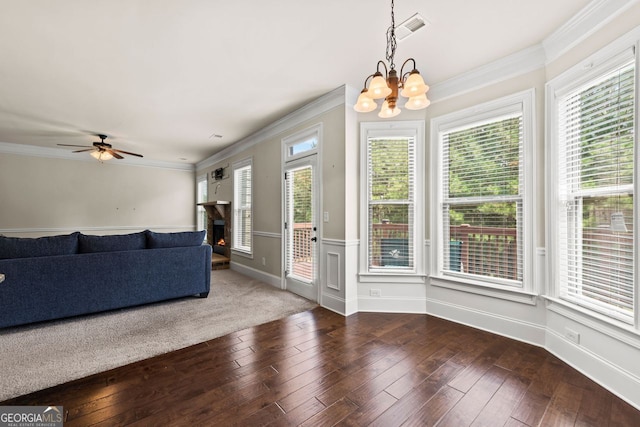 unfurnished living room featuring ceiling fan with notable chandelier, visible vents, a lit fireplace, ornamental molding, and hardwood / wood-style floors