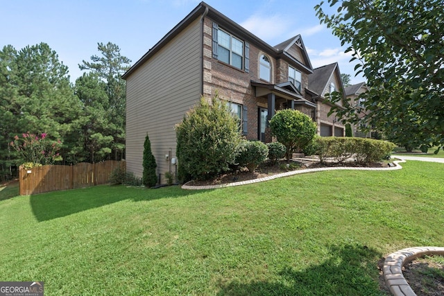 view of side of home featuring brick siding, fence, and a yard