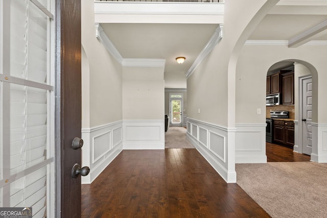 hall featuring crown molding, arched walkways, a decorative wall, and dark wood-style flooring