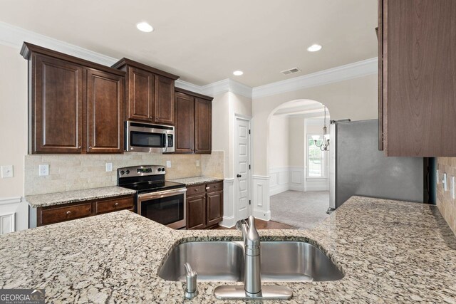 kitchen featuring visible vents, arched walkways, stainless steel appliances, dark brown cabinets, and a sink