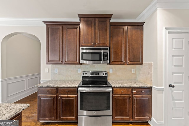 kitchen with appliances with stainless steel finishes, ornamental molding, backsplash, and dark brown cabinets