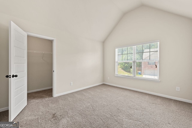 unfurnished bedroom with carpet floors, lofted ceiling, a walk in closet, and baseboards