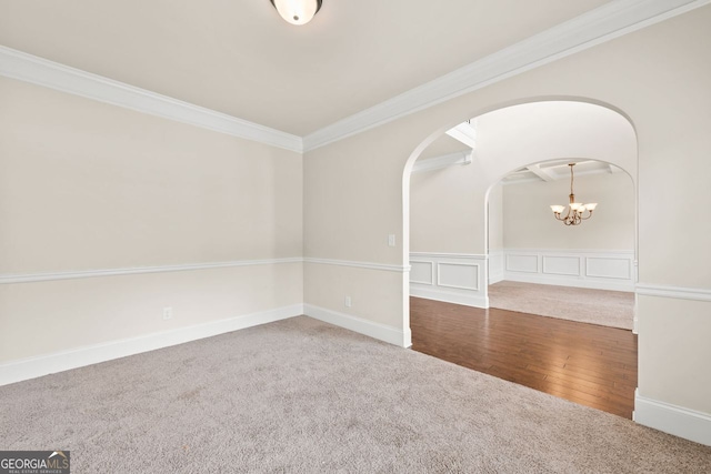 carpeted empty room featuring arched walkways, wood finished floors, an inviting chandelier, crown molding, and a decorative wall