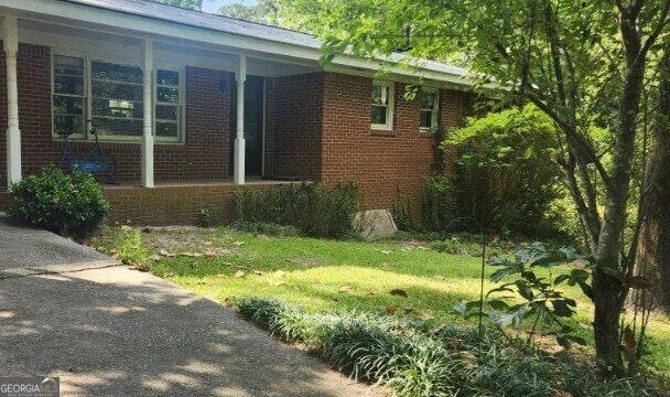 view of side of property featuring brick siding, a lawn, and a porch