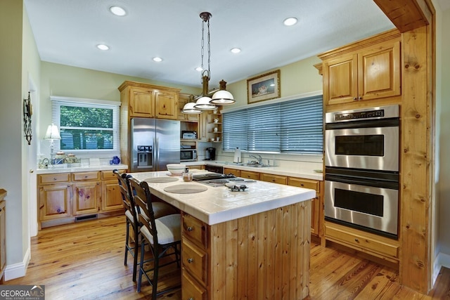 kitchen featuring appliances with stainless steel finishes, tile counters, a sink, and light wood finished floors