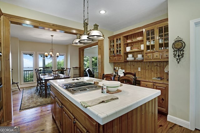 kitchen with tile countertops, wood finished floors, hanging light fixtures, open shelves, and brown cabinetry